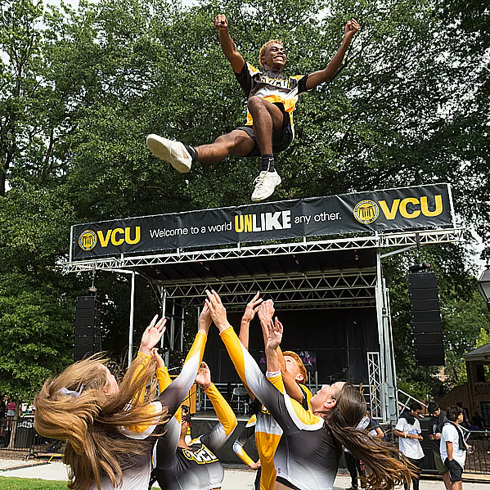 VCU cheerleader smiling while being thrown into the air by a groupd of cheerleaders.