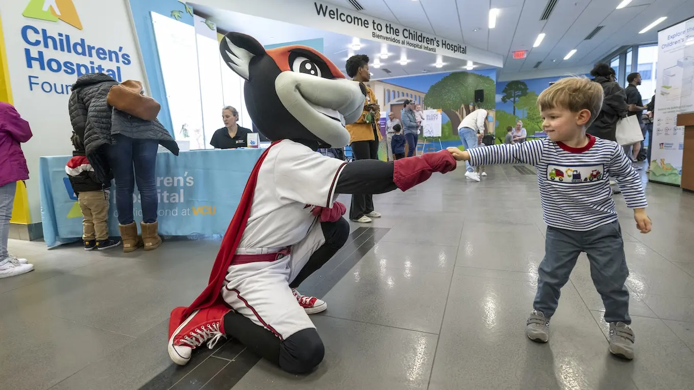 A flying squirrel mascot fist bumps a young child.