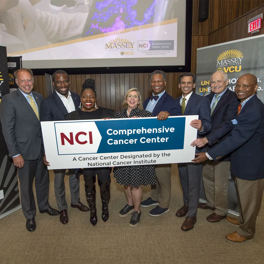 Photo of a group at Massey Cancer Center holding a sign that reads: NCI Comprehensive Cancer Center