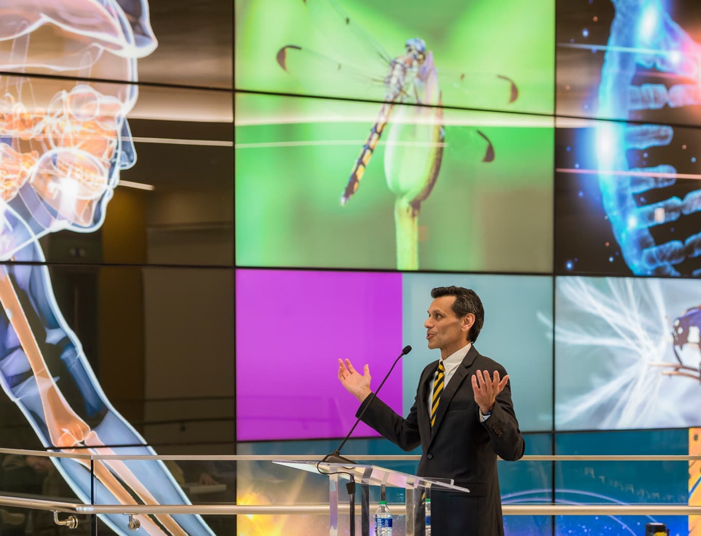 Michael Rao, president of VCU and VCU Health System, speaking at a podium in front of bright STEM-related graphics.