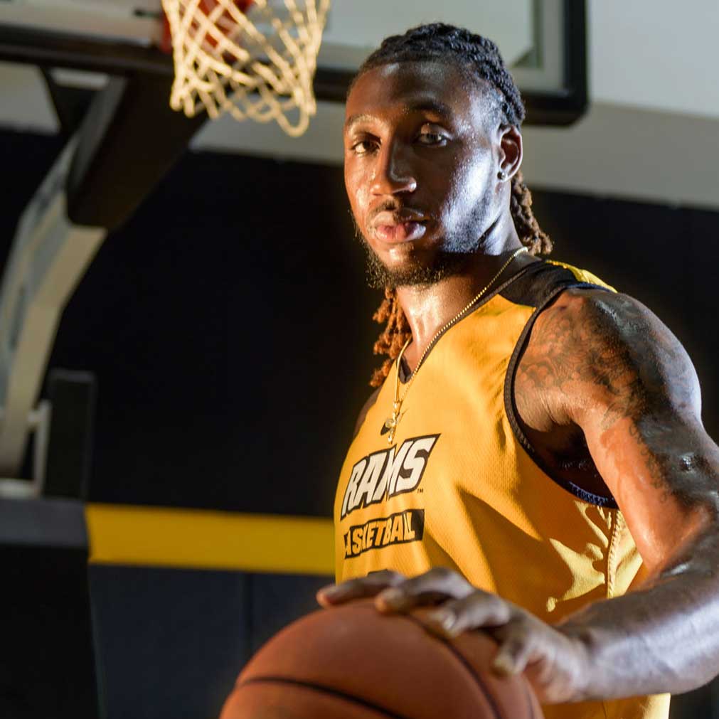 Portrait of VCU basketball player holding a basketball with hoop in the background