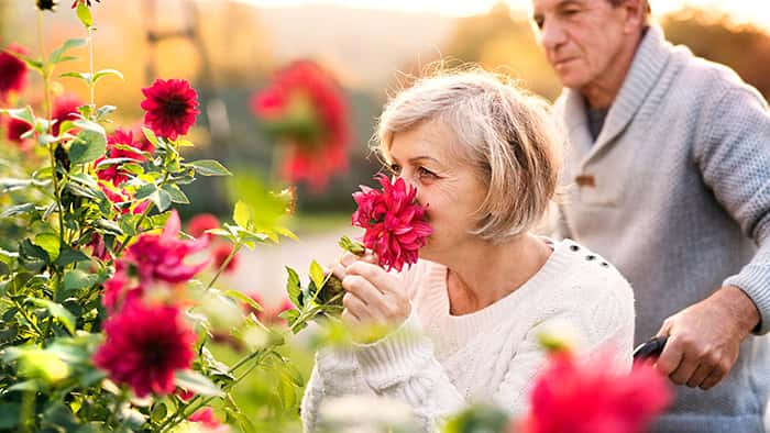 A woman smells a flower as a man stands stands nearby