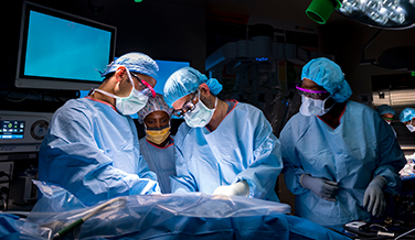 Doctors wearing scrubs preforming a Robotic-assisted transplantation under bright lights.