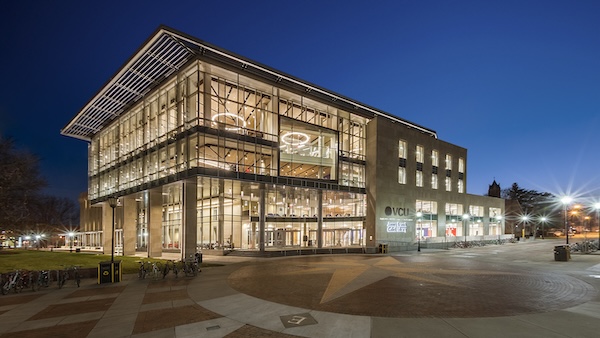 Twilight view of the James Branch Cabell Library at Virginia Commonwealth University (VCU), showcasing its modern glass facade and illuminated interior against the evening sky, with parked bicycles and a pedestrian plaza in the foreground.
