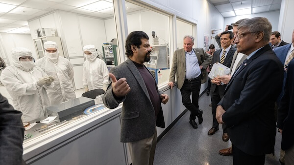 A group of people touring a lab environment attentively listening to a person gesturing during an explanation.