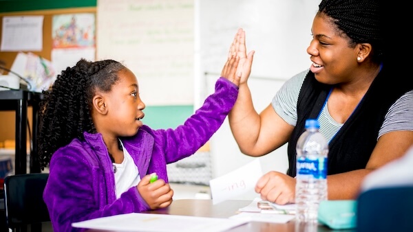 An adult giving a high five to a young student during a classroom activity.