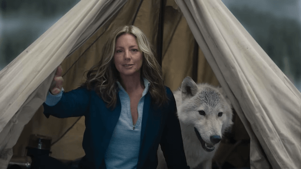 A woman positioned in the center of an open tent with a white and gray wolf standing behind her.