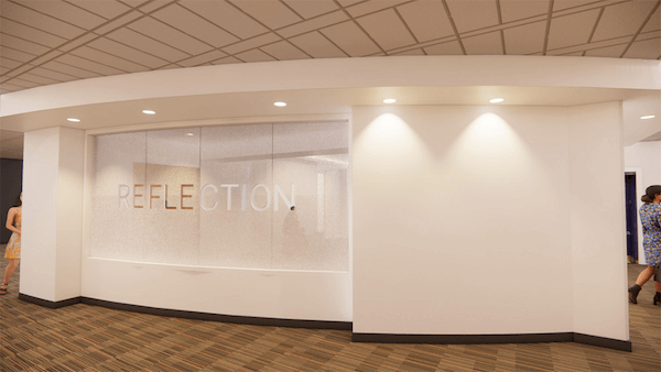 A white wall featuring a glass panel with the word "REFLECTION" written in white lettering.